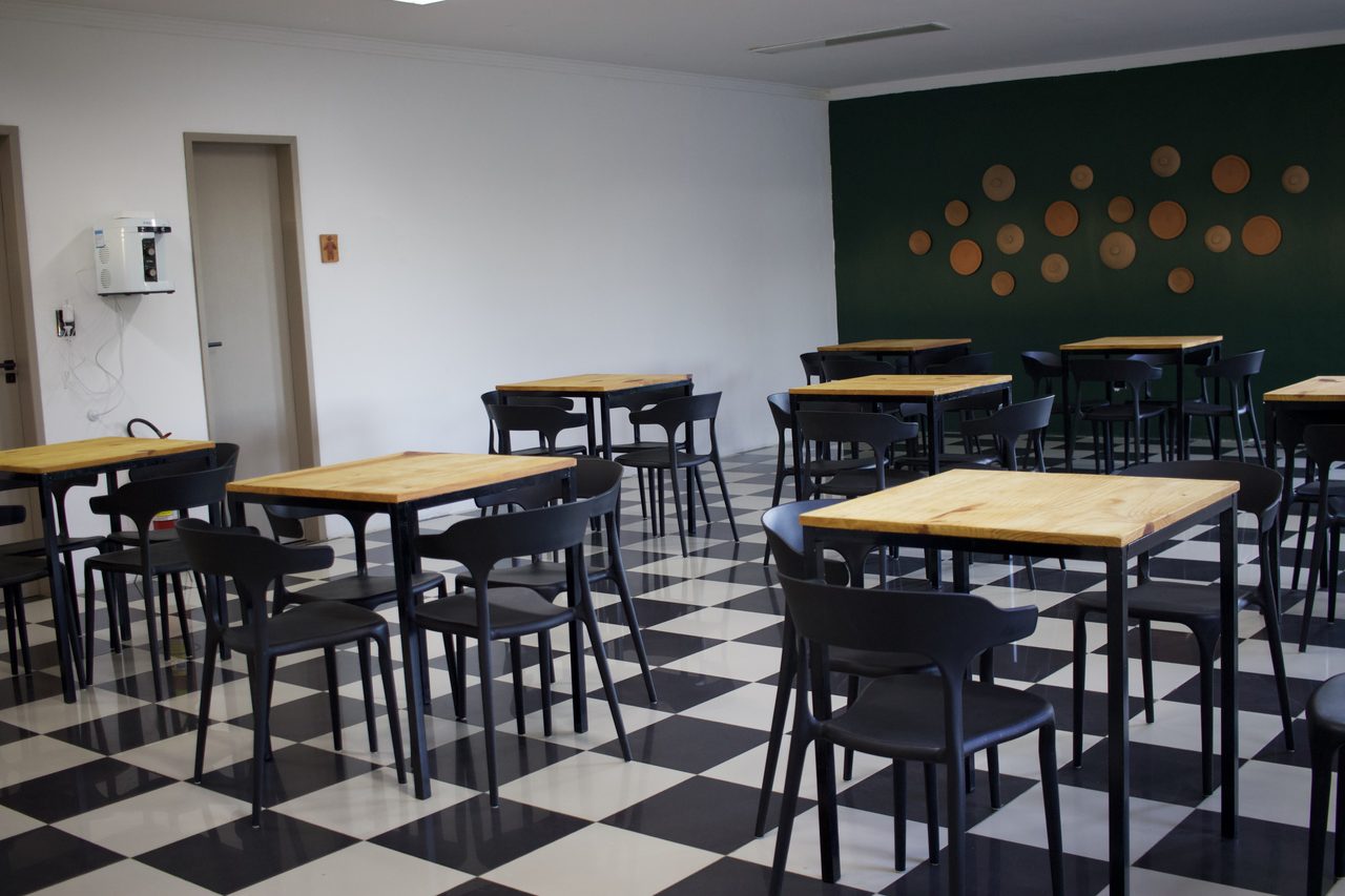 Salão de café da manhã com piso xadrez, mesas de madeira e parede verde escuro