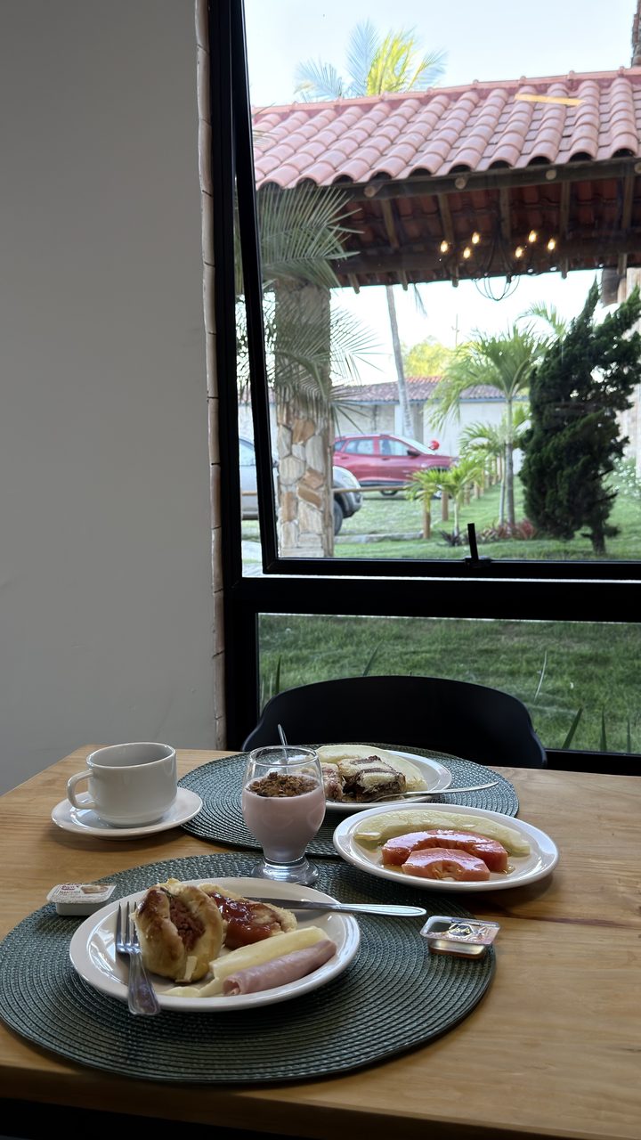 Mesa do café ao lado da janela, com vista para o pórtico e as palmeiras do jardim