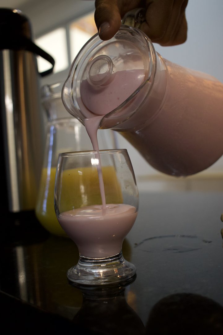Vitamina sendo servida em uma taça, ao lado da jarra de suco de laranja