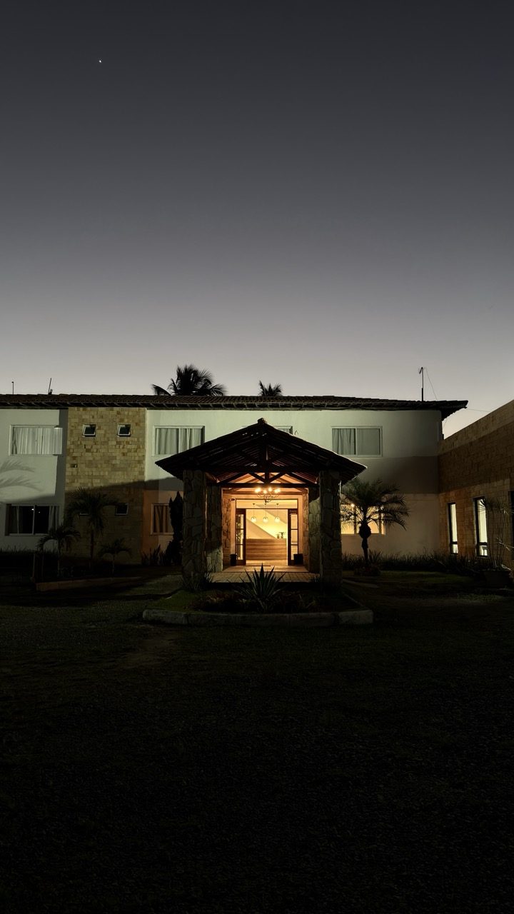Pórtico de madeira do hotel iluminado ao anoitecer, visto do jardim