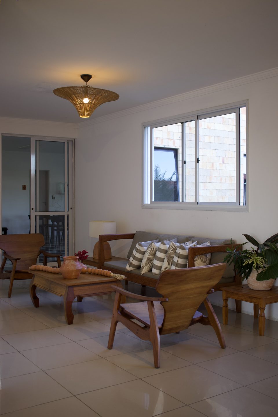 Sala de estar com poltronas e mesa de centro de madeira maciça, luminária de palha e plantas